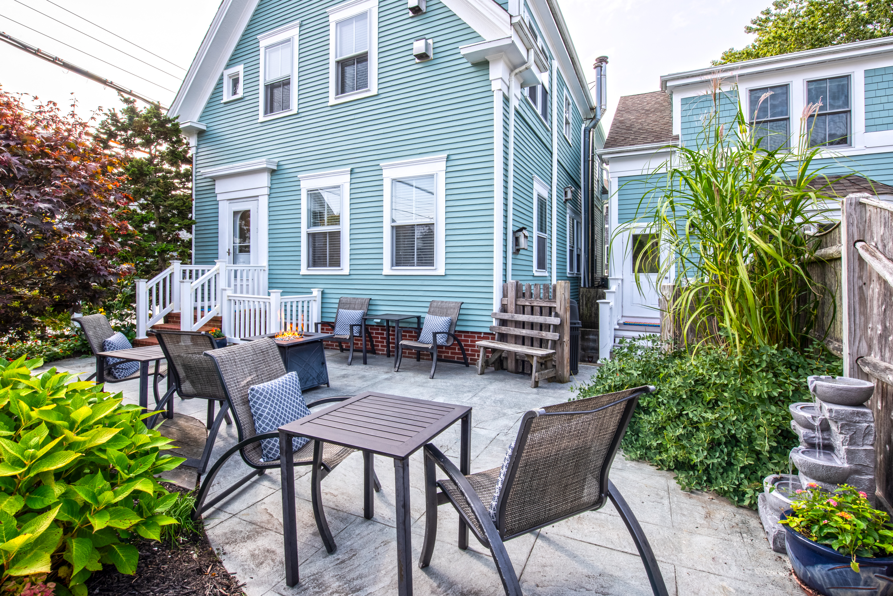 A patio area with outdoor furniture and a fire table in front of a blue house.