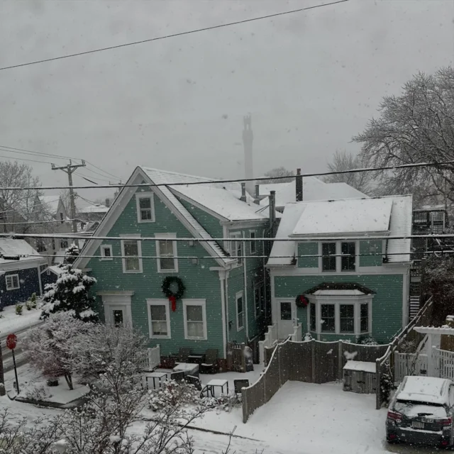 A snowy exterior view of a house with a fence and a car parked outside.